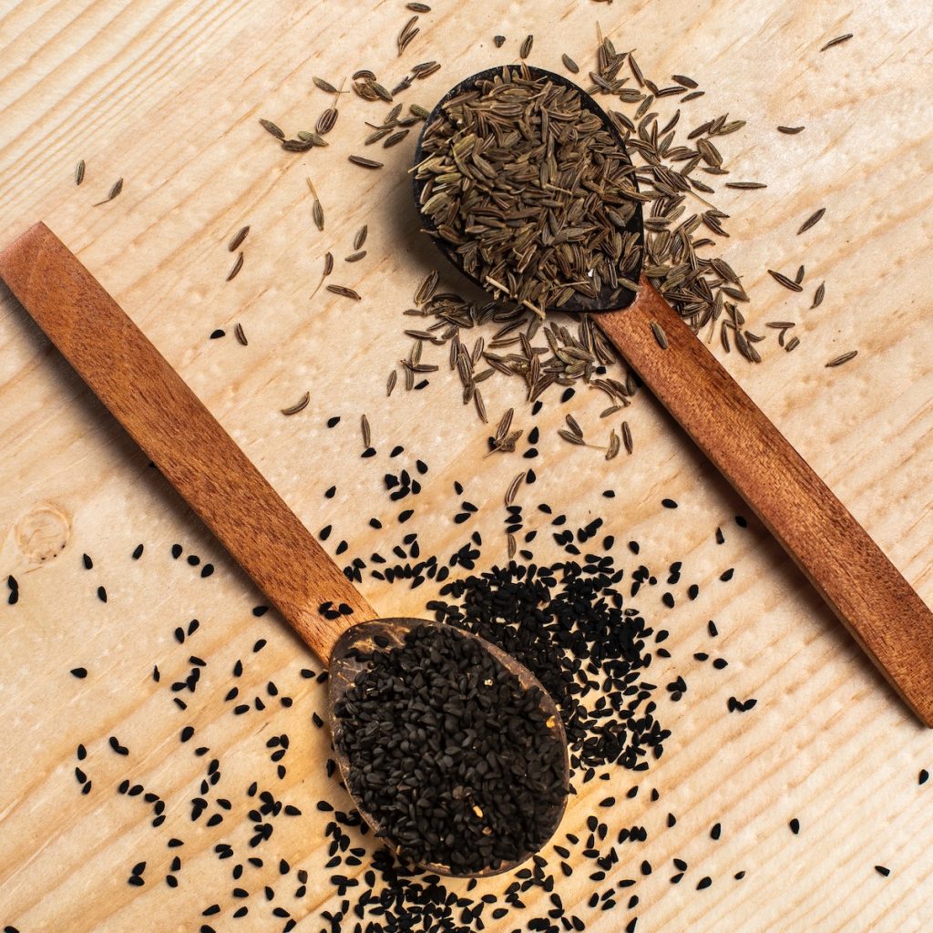 Black sesame seeds and nigella seeds on wooden spoons