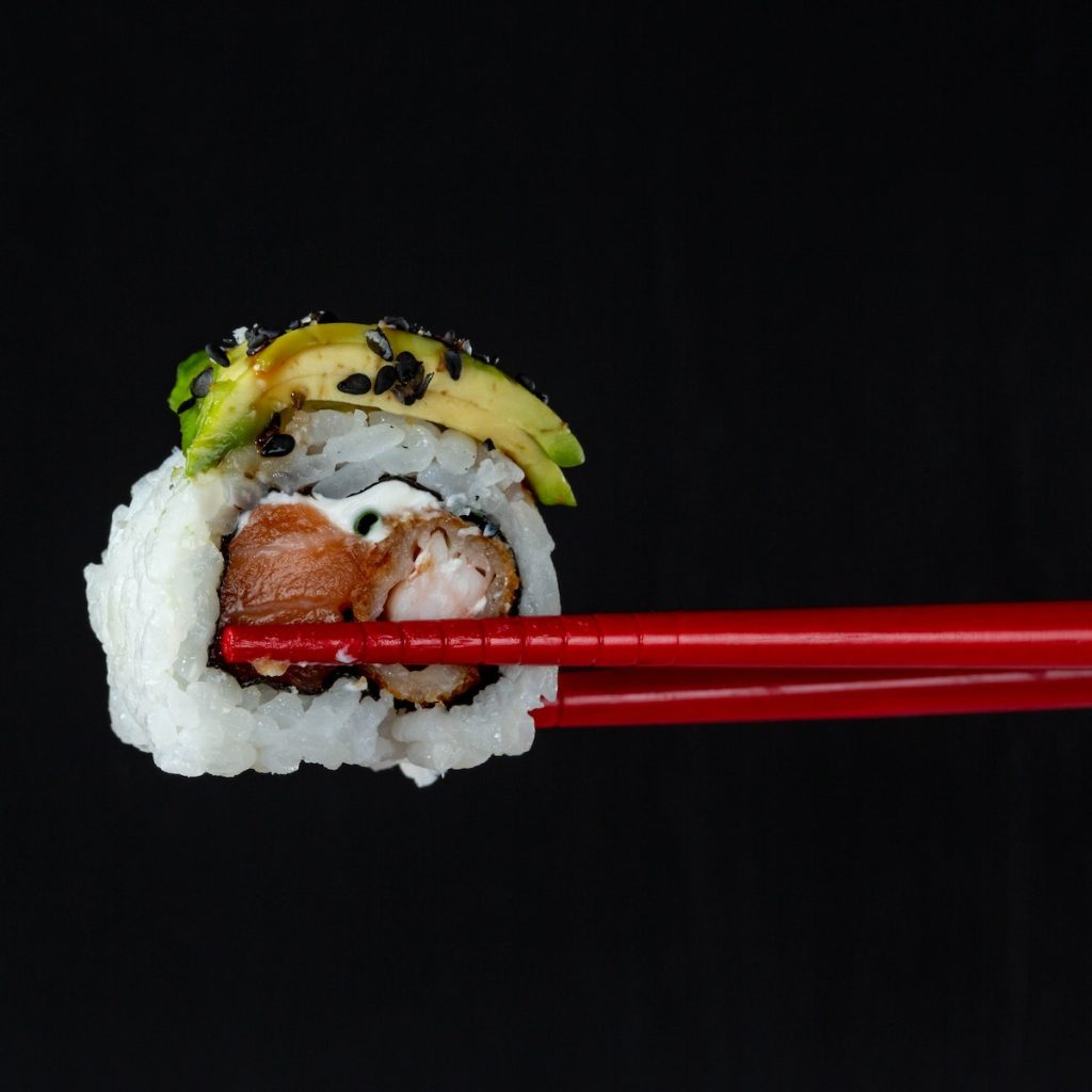 Close-up photo of sushi with black sesame seeds between chopsticks