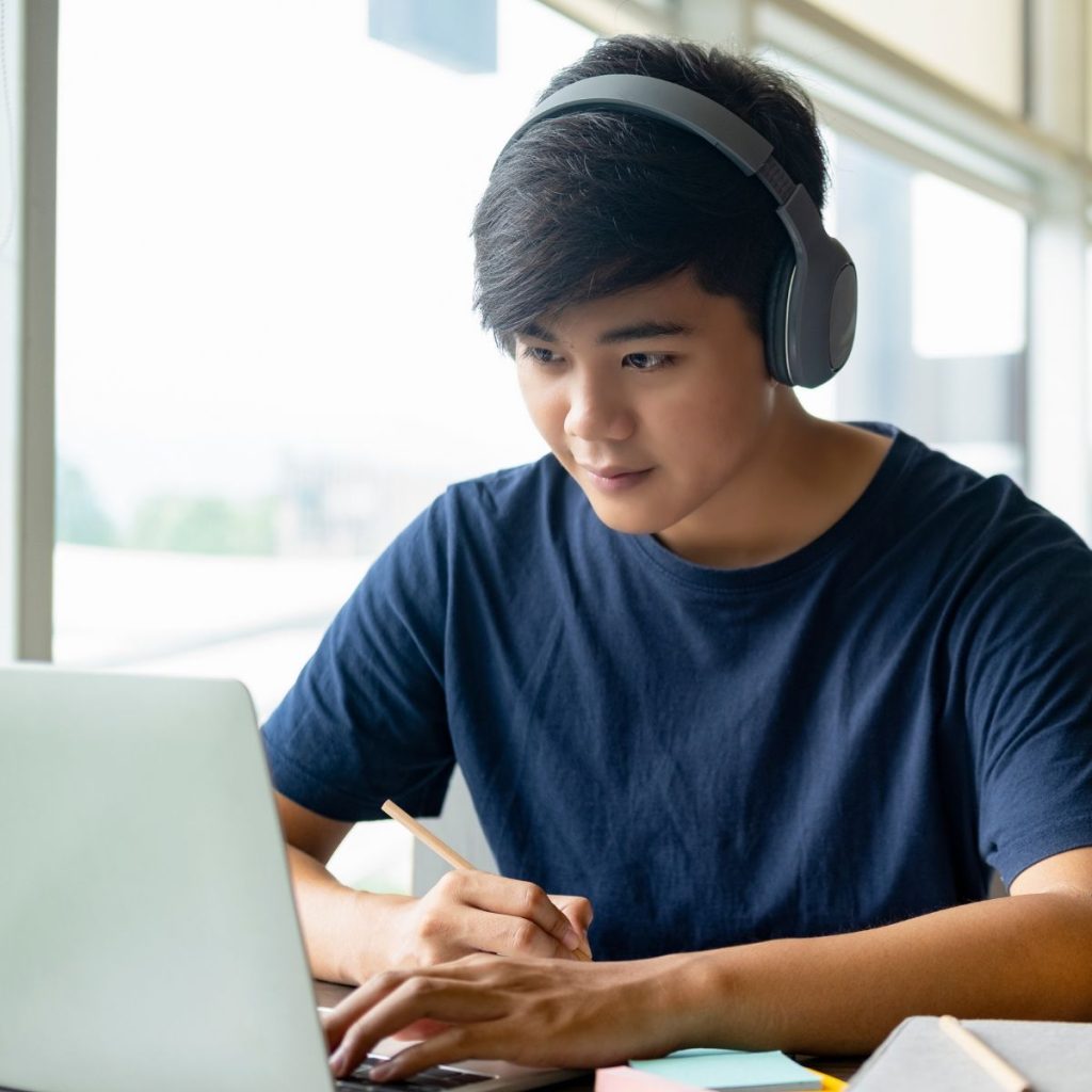 Male student using laptop while wearing headphones