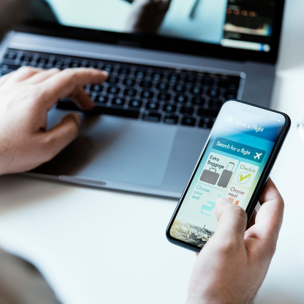 Person booking a flight while using phone and laptop