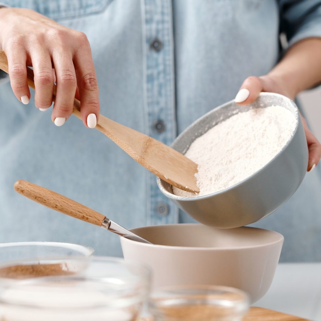 Person using a wooden spoon to add flour to the bowl