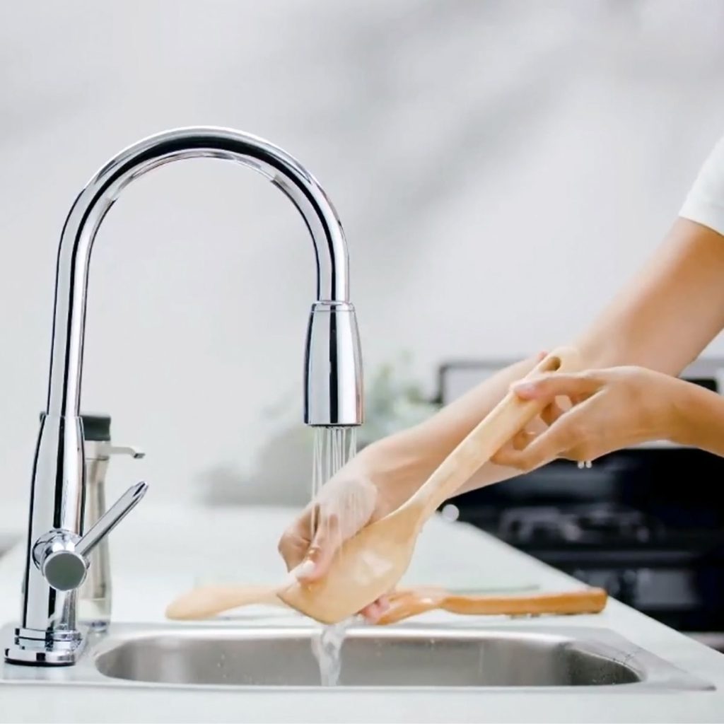 Person washing a wooden spoon in the faucet