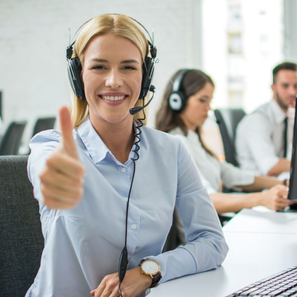 Smiling customer support agent woman showing thumb up in call centre