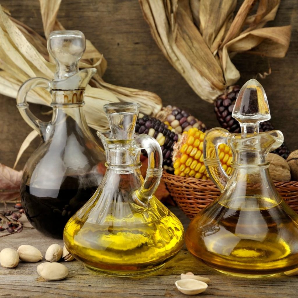 Three bottles of cooking oil rest on the table with their fruit and seed sources.