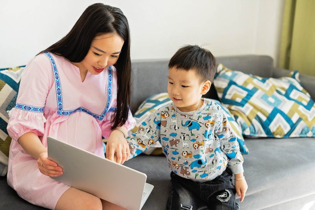 a pregnant mother and her son looking at the laptop