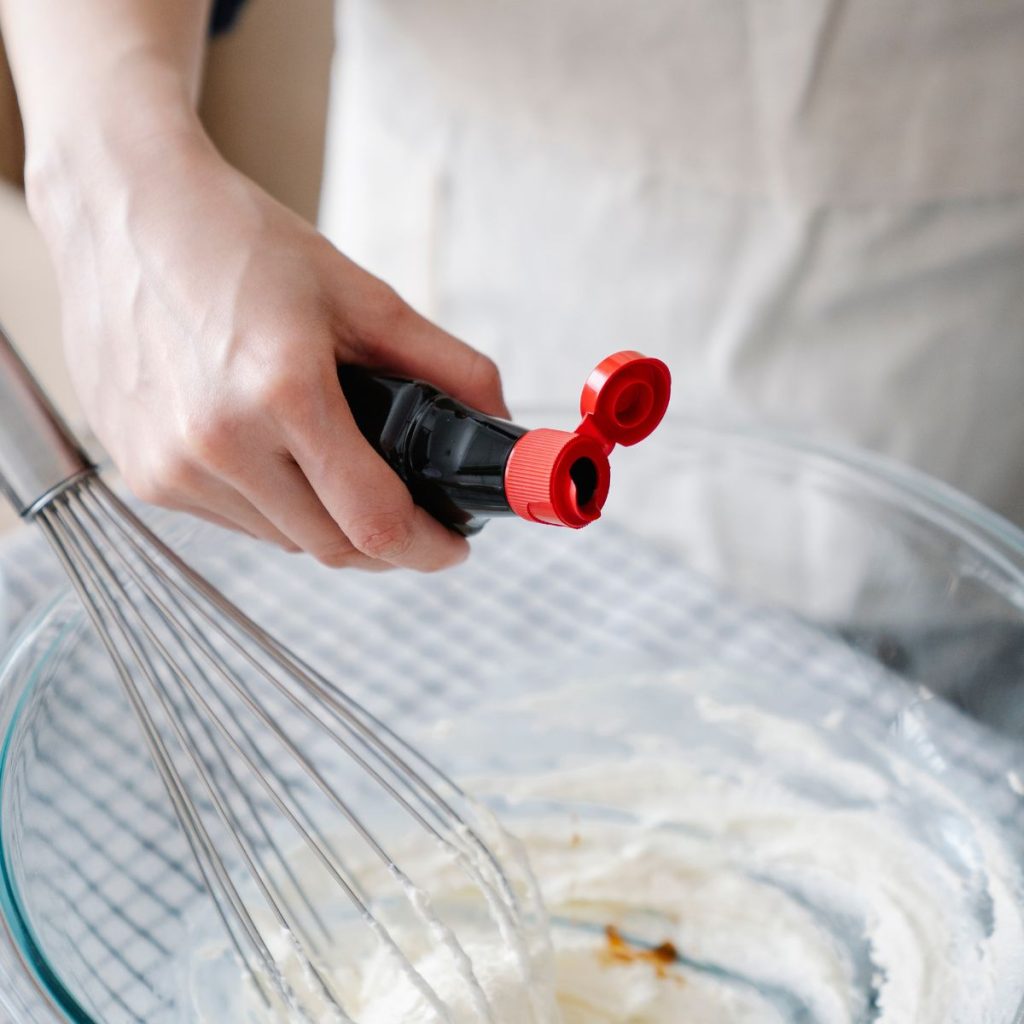 A hand putting vanilla extract into a bowl