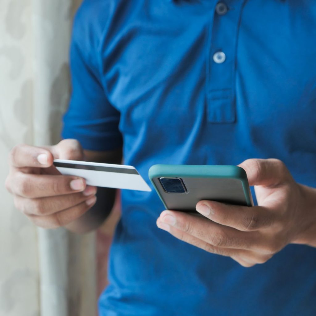 Man in blue polo shirt using a smartphone and a credit card