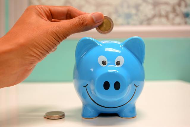 a hand inserting a coin into a piggy bank