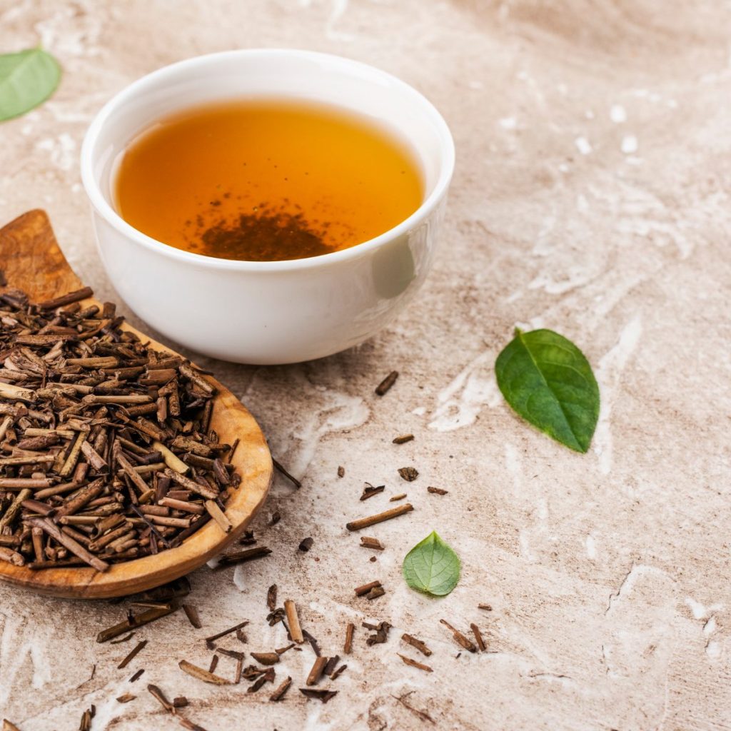 hojicha tea in a cup with its dried leaves on the side