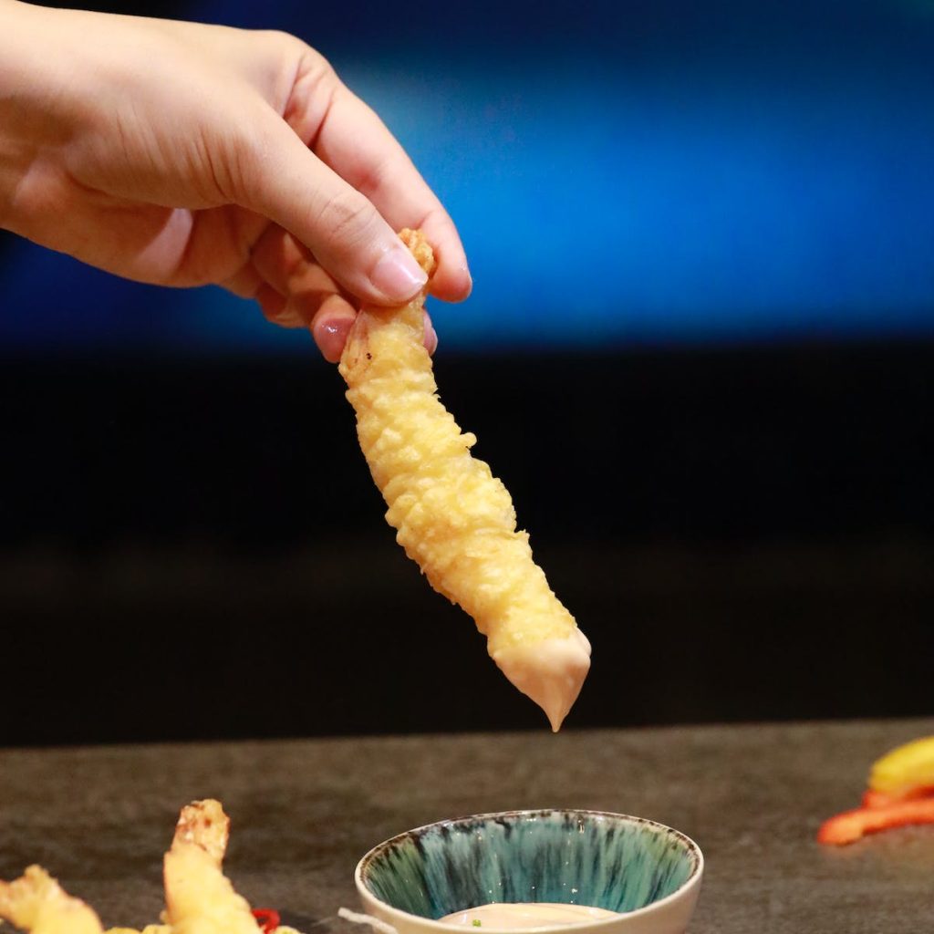 lady holding a tempura and dipping in a Japanese mayonnaise