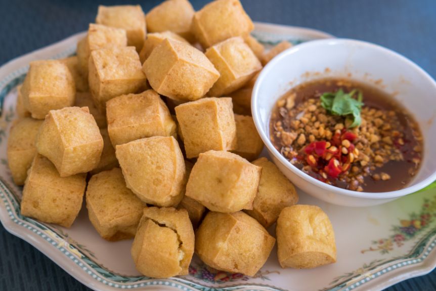 Japanese agedashi tofu on a plate with dip on the side.