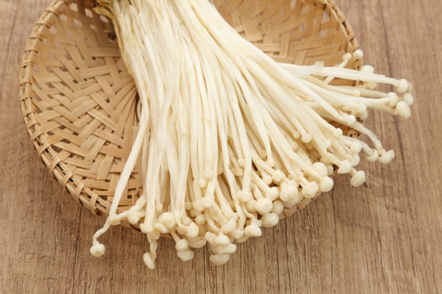 Enoki Japanese mushrooms in a basket on top of a wooden board.